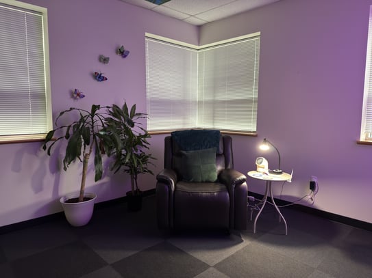 A sensory room that includes low, ambient lighting, a reclining chair, and plants.