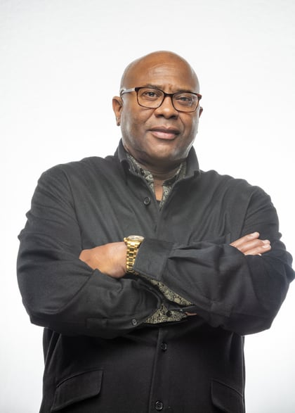 Michael Holton wears a black button down with a gold watch and glasses