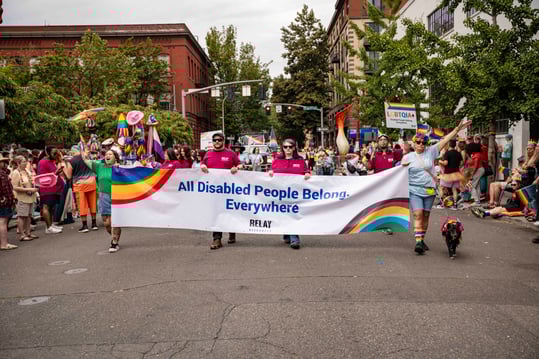 Relay team carrying a banner in the Portland Pride Parade that says All Disabled People Belong. Everywhere.