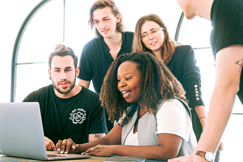 A woman shows her coworkers something on her laptop. Photo by Canva Studio. 