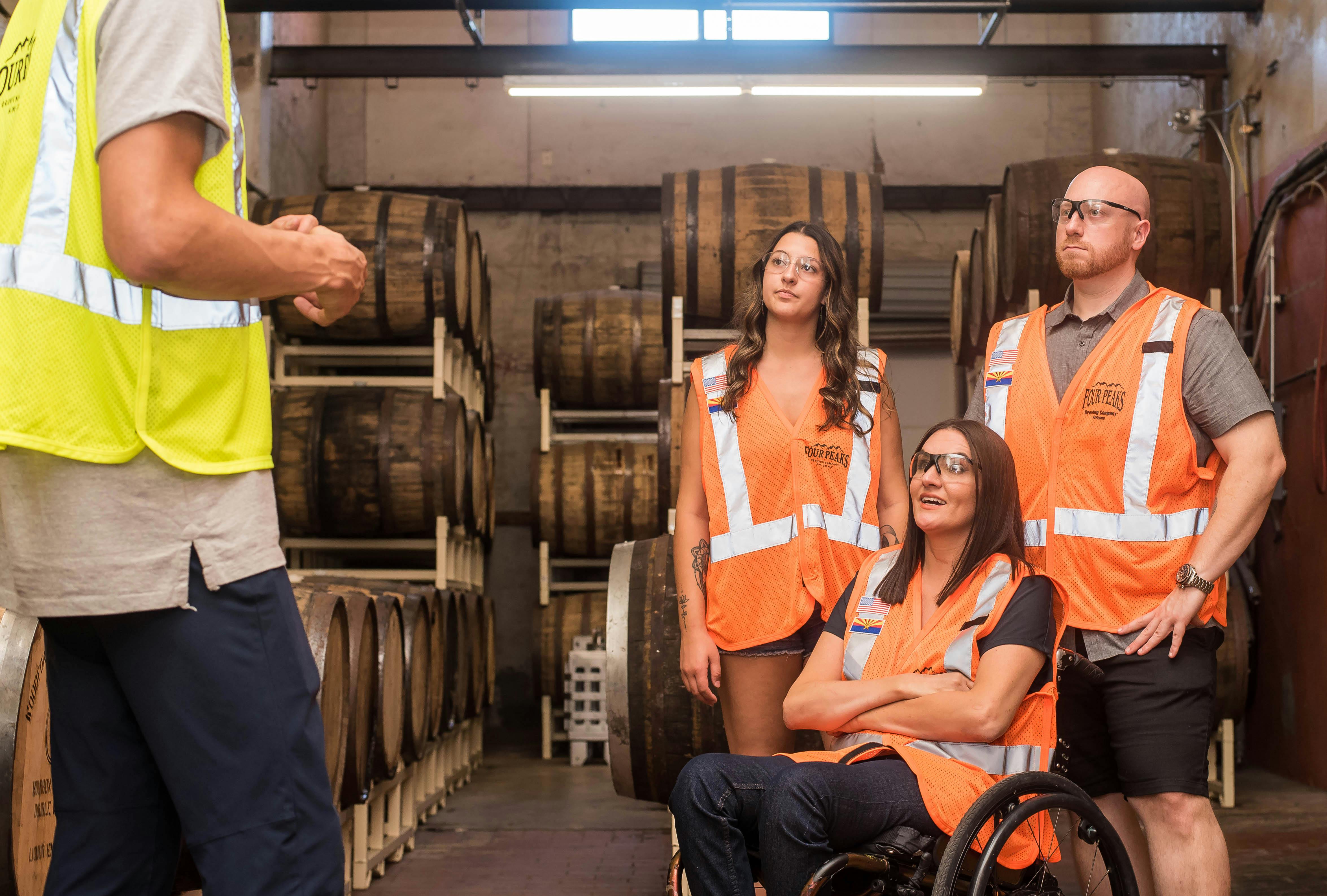 People in reflective vests in a warehouse, one in a wheelchair, stand in a circle 
