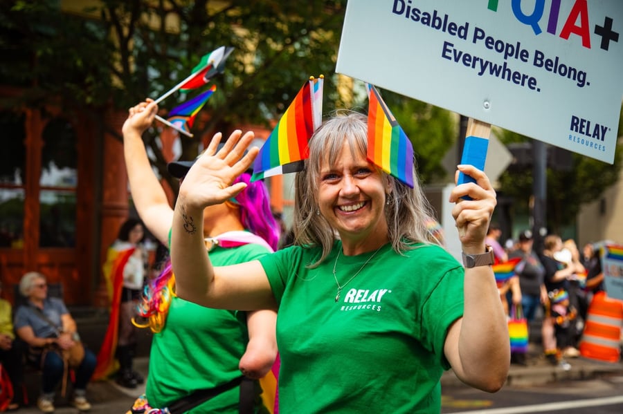 A lady in grey hair with a green Relay Resources shirt waves at the Pride 